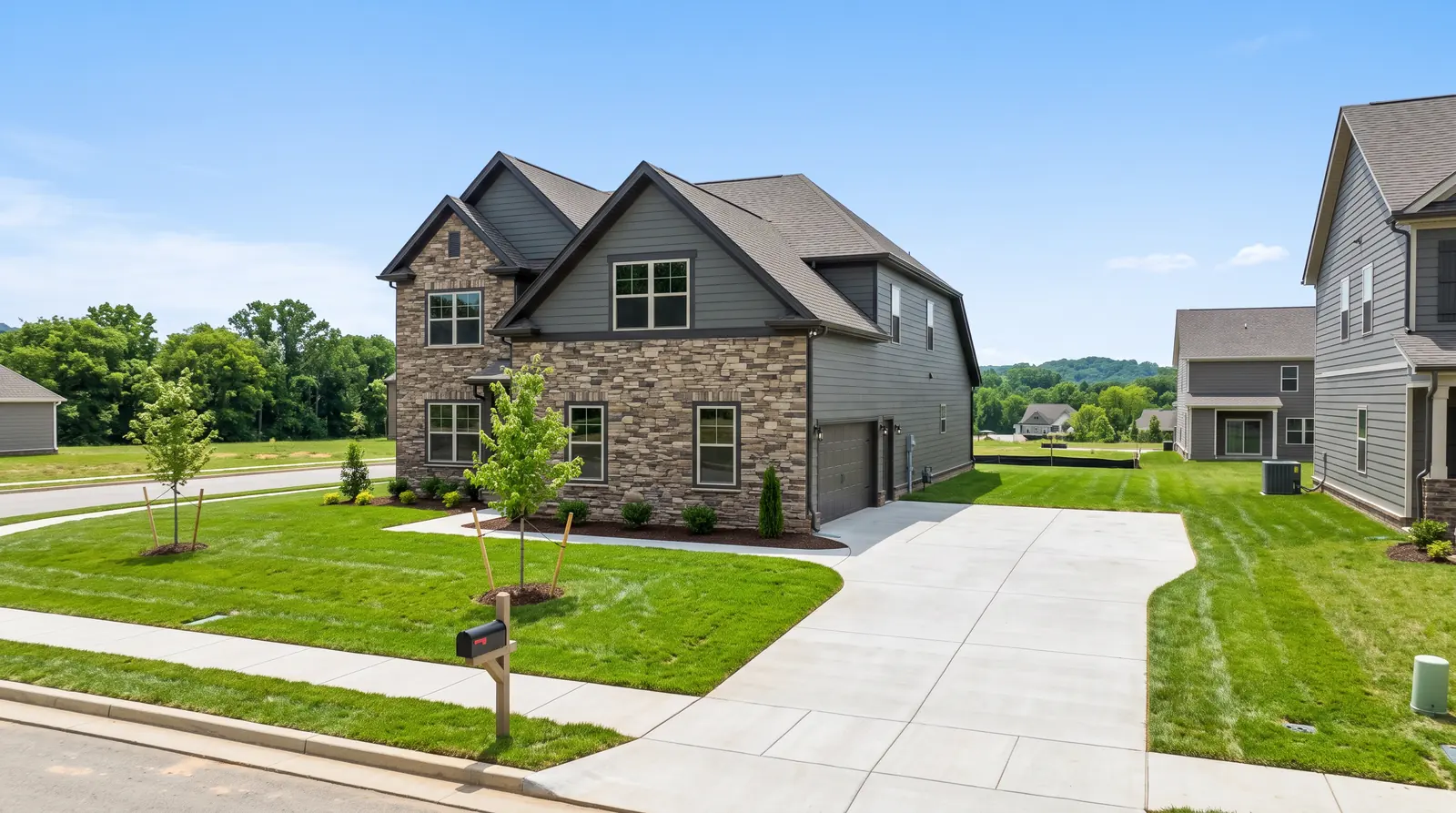 A newer two-story stone-and-siding home in a new Tennessee neighborhood with fresh sod, young trees, a tidy driveway and another house framing in the background